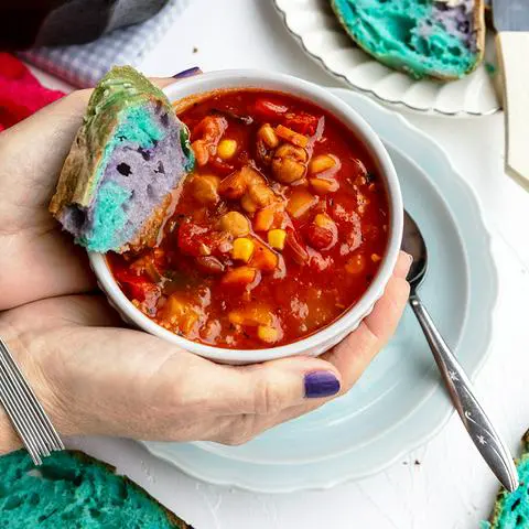 Robin holding a bowl of Panera’s 10 vegetable soup with a piece of colorful bread in it
