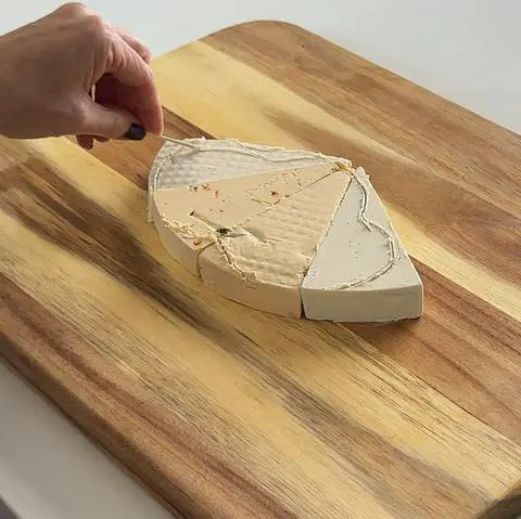 tracing the shape of the dog emoji onto the cheese wedges using a toothpick.