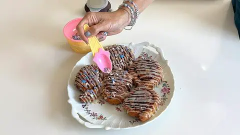 adding vegan sprinkles to cinnamon rolls.