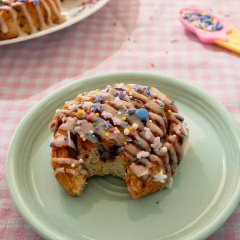 a vegan cinnamon roll on a seafoam green plate with a bite taken out of it.