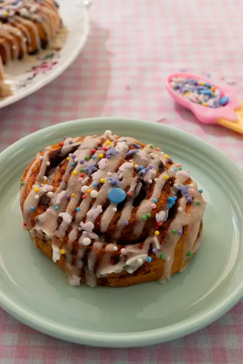a vegan cinnamon roll with icing and sprinkles on a seafoam green plate.