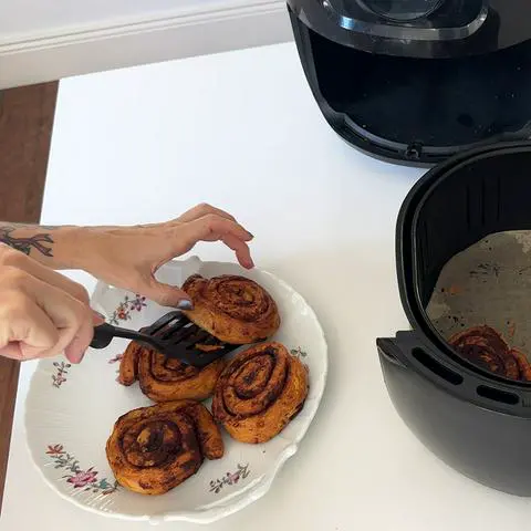 transferring cinnamon rolls from air fryer basket to a plate.