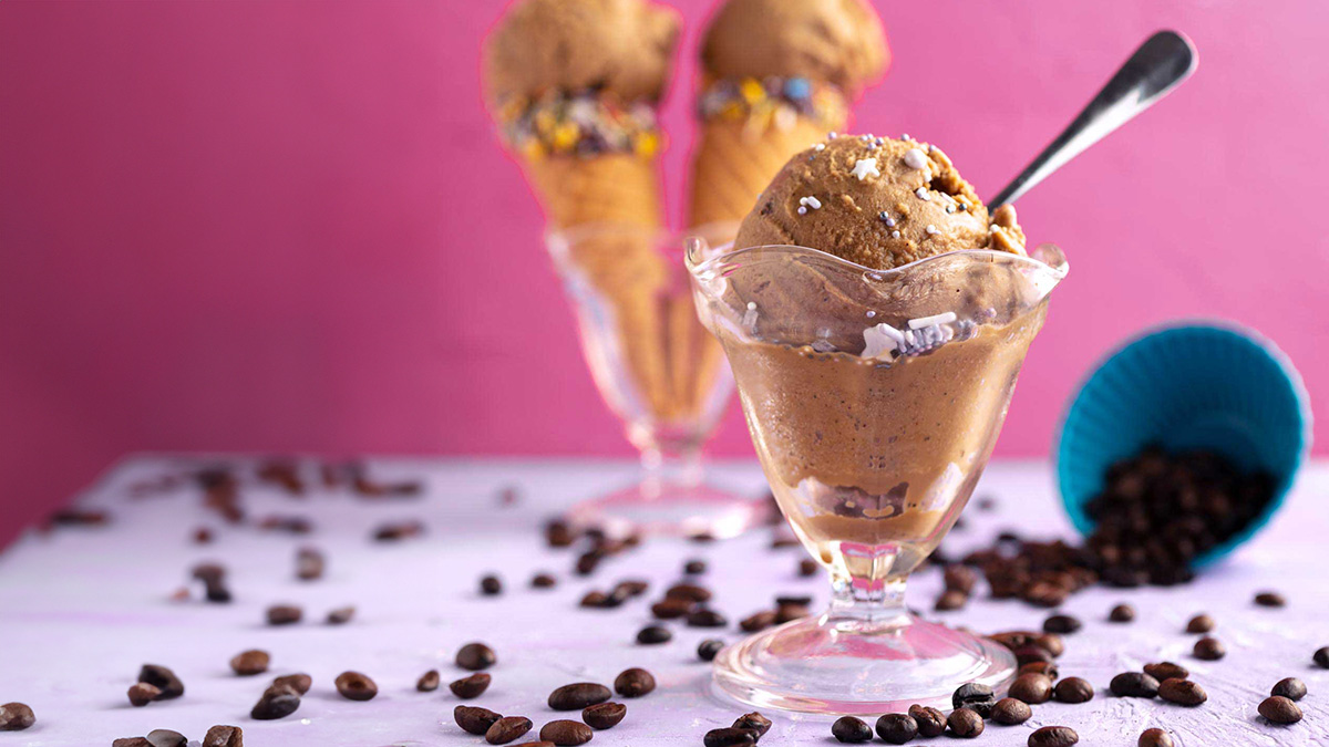 old fashioned ice cream dish with a scoop of vegan coffee ice cream and 2 ice cream cones in the background.