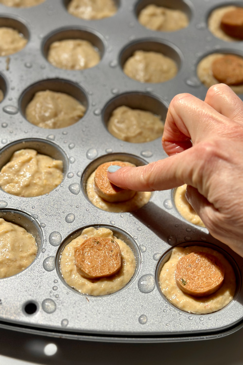poking pieces of vegan hot dogs into the cornbread batter
