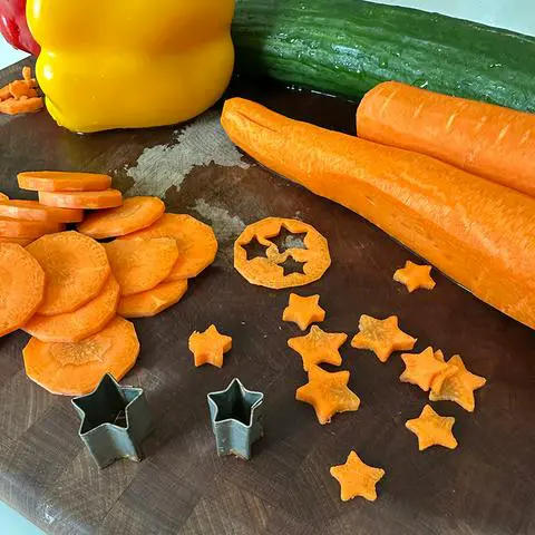 a cutting board with veggies and carrots cut into star shapes.