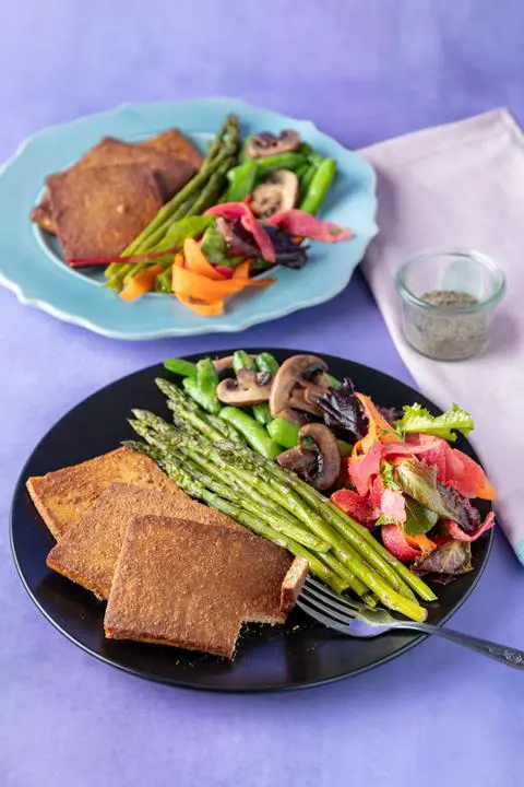 vegan ham slices on a plate with veggies and salad.
