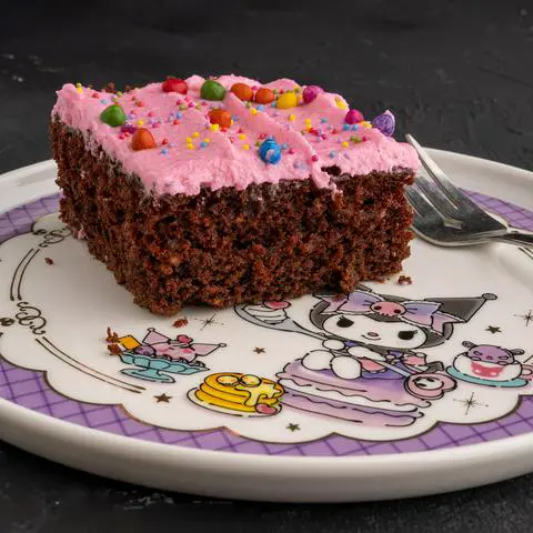 a slice of a single-layer vegan chocolate sheet cake with pink frosting and rainbow candy sprinkles on a kuromi plate.