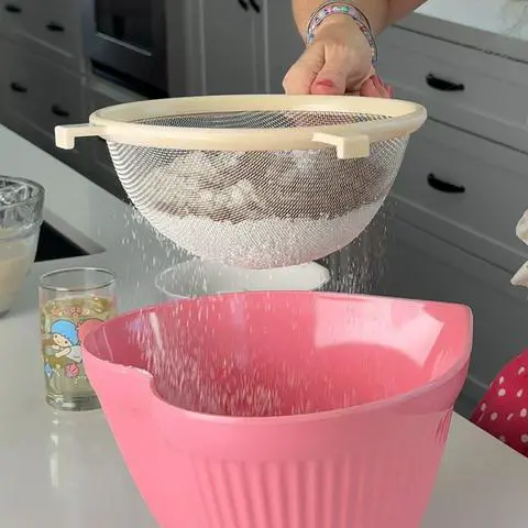 sifting dry ingredients into a pink bowl.