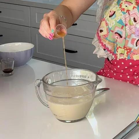 pouring apple cider vinegar into nondairy milk to make vegan buttermilk.