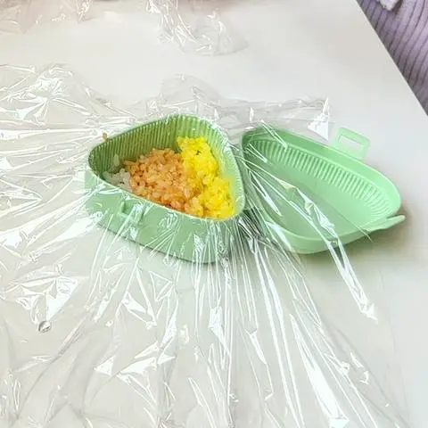 onigiri mold with cling wrap and the bottom layer of rice.