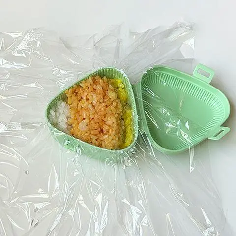 onigiri mold with cling wrap, the bottom layer of rice, the tuna filling layer, and the top layer of white and orange rice.