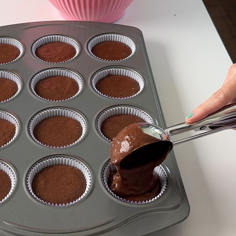 scooping gluten-free vegan chocolate cake batter into the cupcake papers.