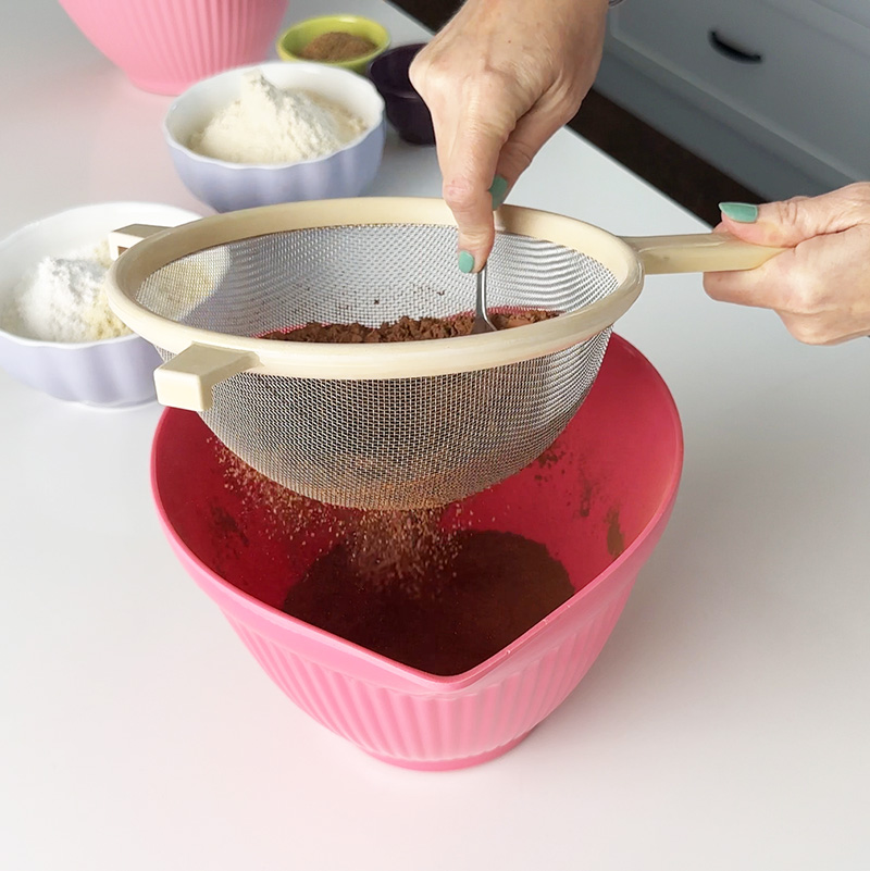 sifting the dry ingredients into a pink heart bowl.