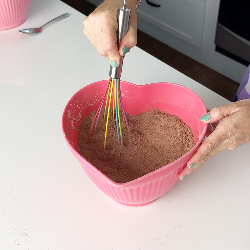 whisking the dry ingredients with a rainbow whisk in a pink heart bowl.