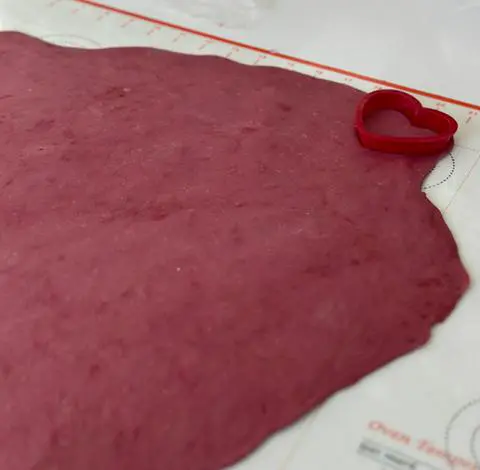 rolling pink pasta dough by hand