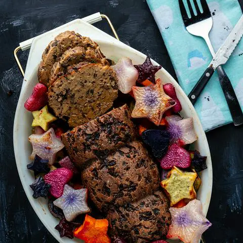 vegan roast surrounded by colorful root veggies in a vintage oval pyrex.