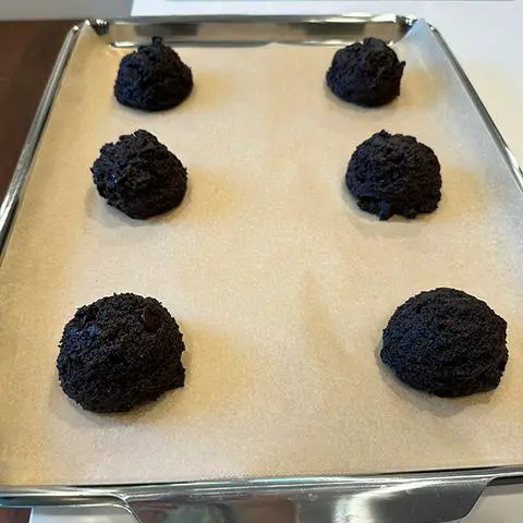 6 cookie dough balls on a baking sheet covered in unbleached parchment paper.