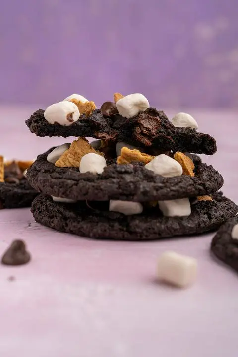 a stack of dark chocolate s’mores cookies, where the top cookie on the stack is just half a cookie showing the inside.