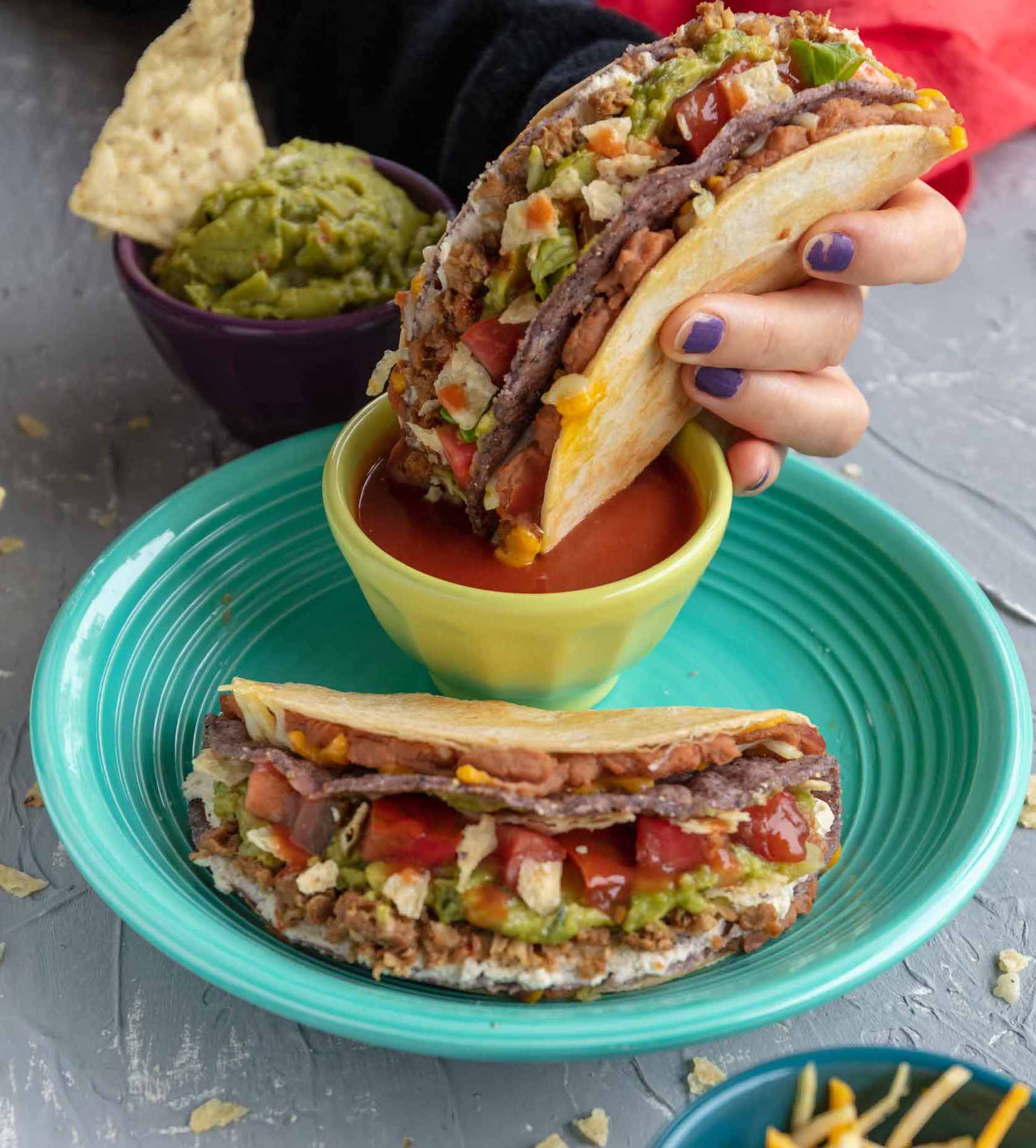 dipping a vegan stuffed grilled taco into a small bowl of hot sauce