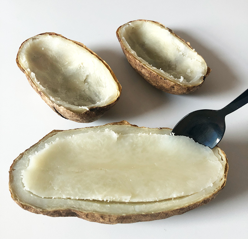 scooping baked potato out of a potato skin shell