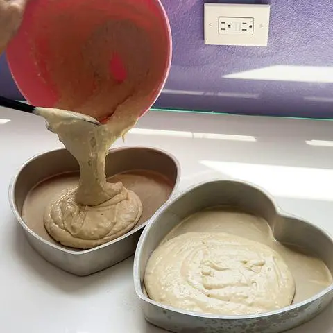 pouring vegan vanilla cake batter into 2 heart shaped cake pans.