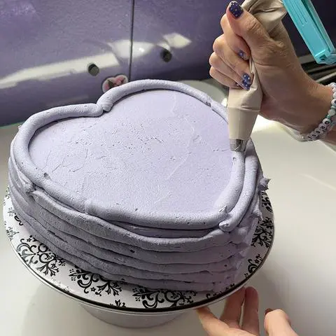 piping rings of frosting on the sides and top of the heart cake.