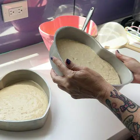 tilting a heart shaped cake pan with batter in it.